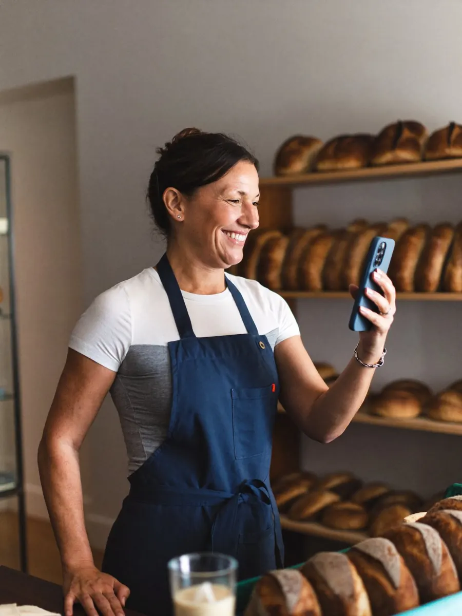 Smiling bakery owner behind her counter, checking her phone