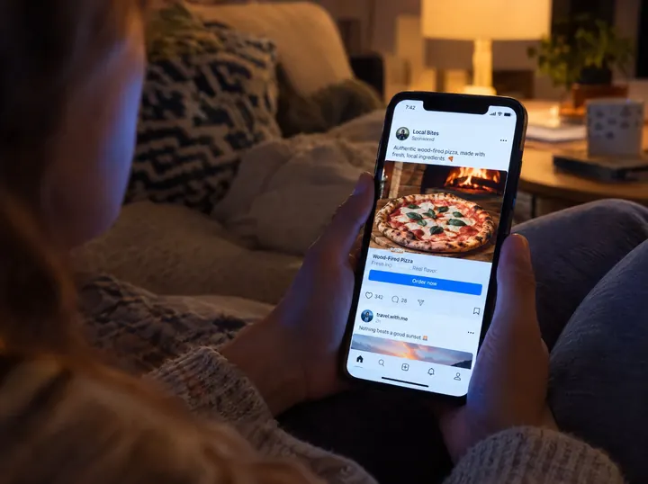 Person on a couch scrolling past a local pizzeria's ad on social media